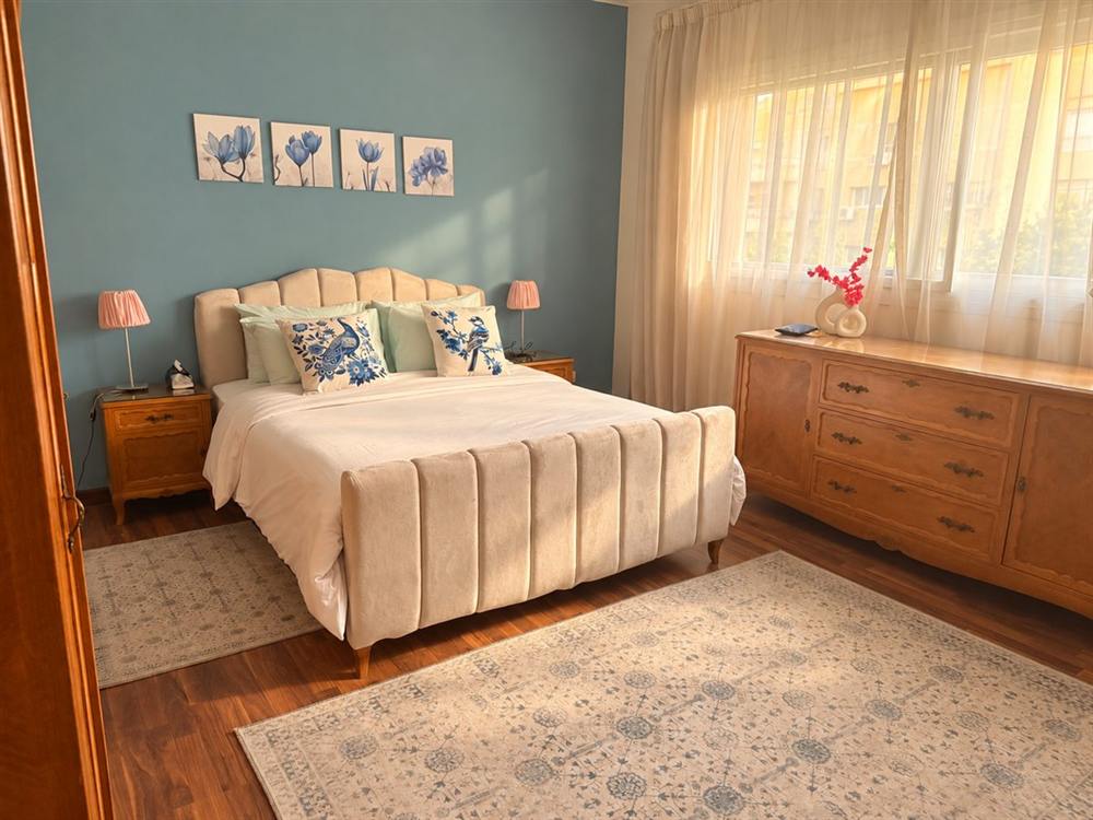 Master bedroom with a blue wall, beige upholstered bed and vintage dresser