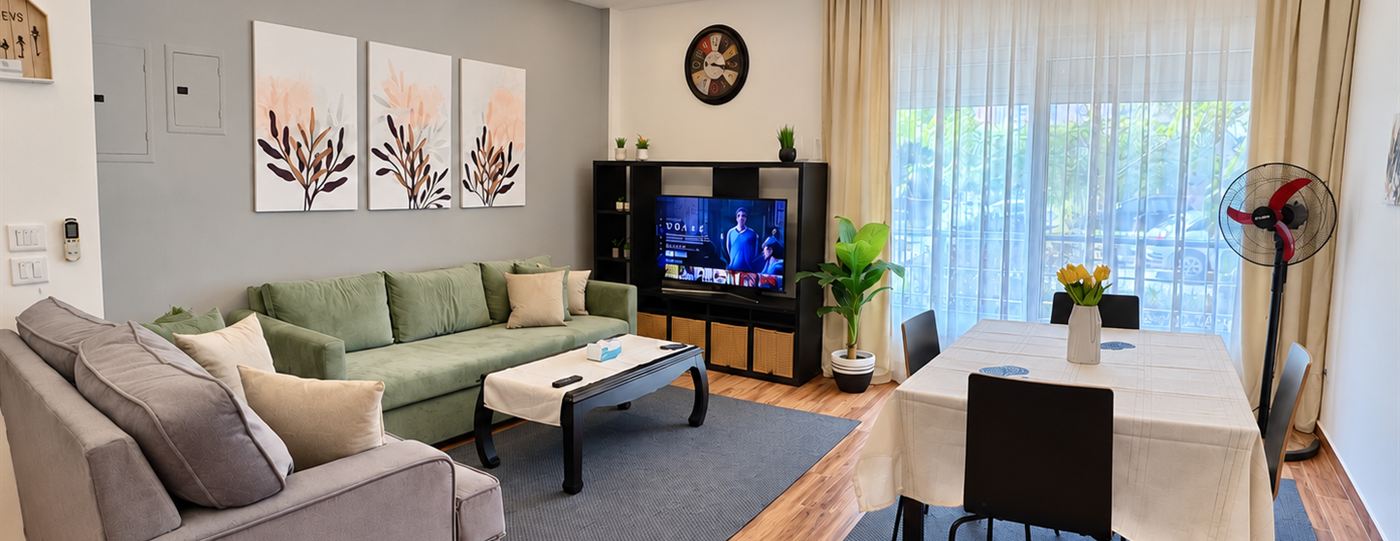 Living and dining area with a sofa, dining table, Smart TV and tall windows