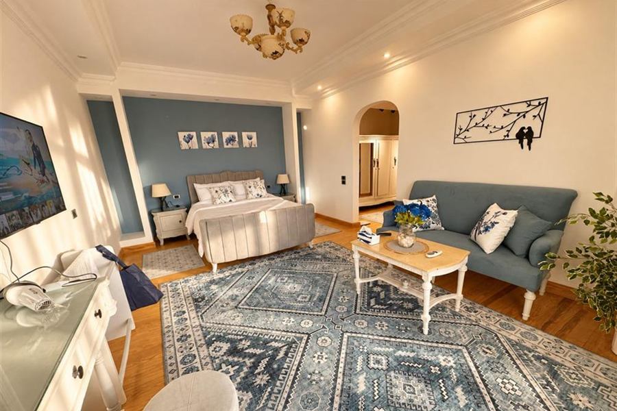 Sunlit main bedroom with an upholstered bed, a blue feature wall and its own sitting area