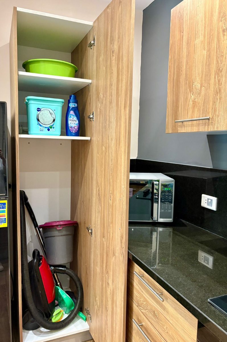 Cupboard beside the fridge holding cleaning supplies and a vacuum cleaner