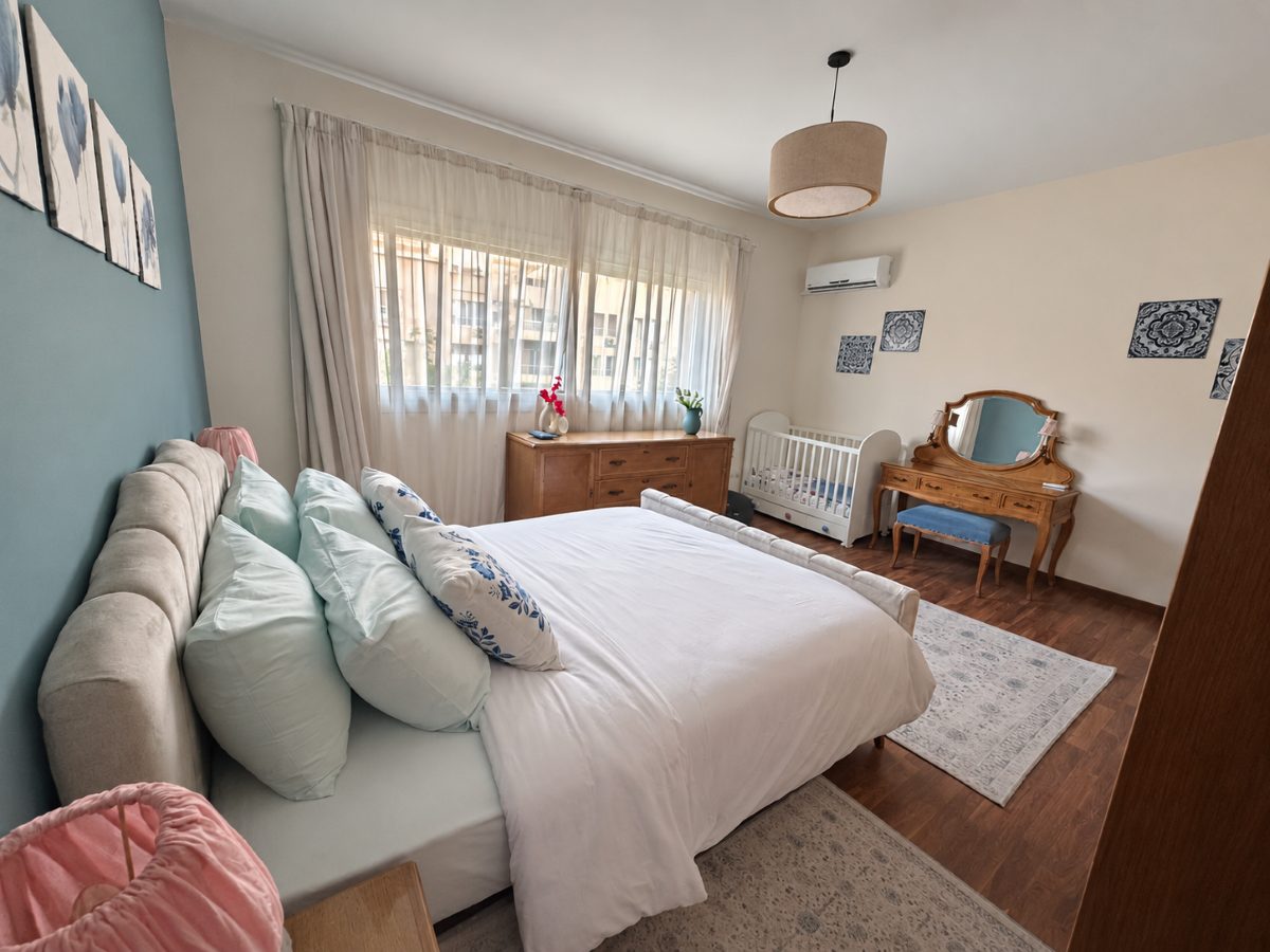 Main bedroom with a mirrored dressing table and a crib beside the bed