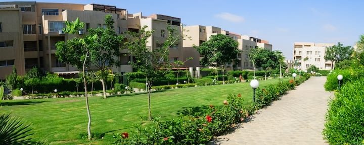 Shared green spaces around the compound, separate from the apartment’s private balcony.