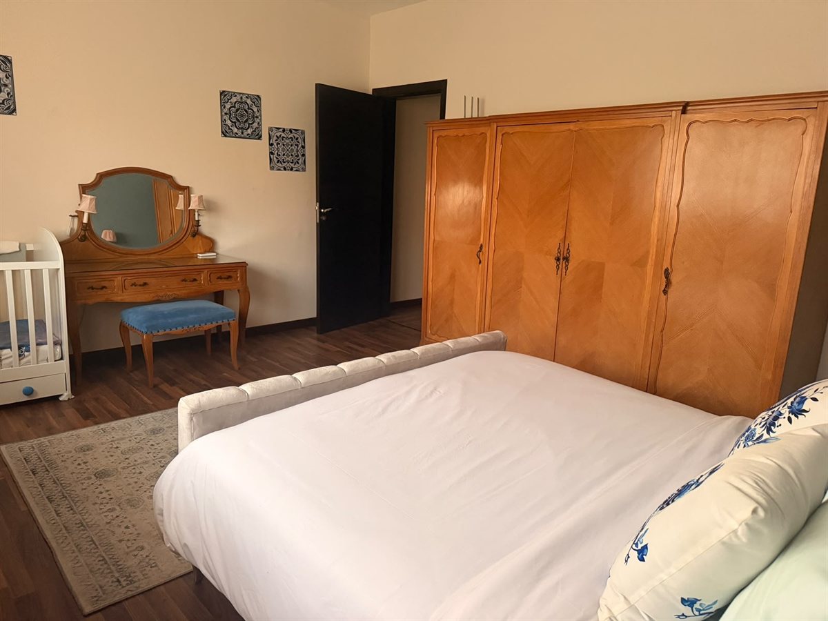 Main bedroom seen from the far side, with a wooden wardrobe, a mirrored dressing table and a crib beside it