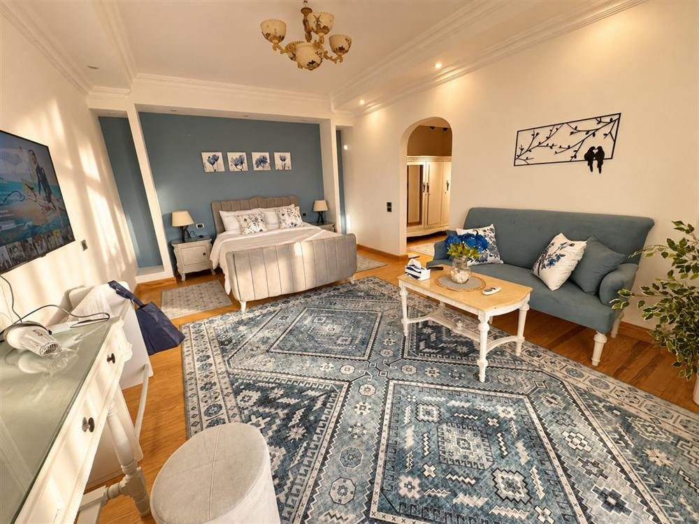 Sunlit main bedroom with an upholstered bed, blue feature wall and a sofa with a coffee table