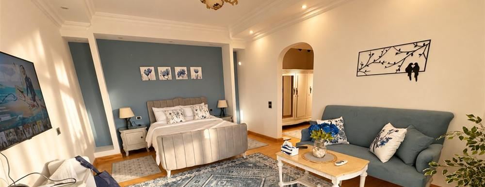 Sunlit main bedroom with an upholstered bed, a blue feature wall and its own sitting area