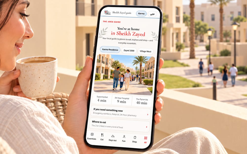 A guest on a sunlit balcony with a cup of coffee, reading the Sheikh Zayed guide on her phone